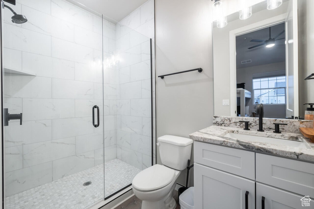 Bathroom featuring a shower with shower door, ceiling fan, toilet, and large vanity