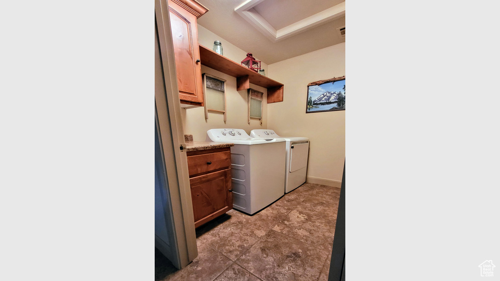 Clothes washing area with dark tile floors, cabinets, and washer and dryer