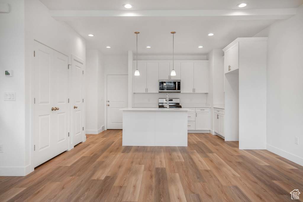 Kitchen with stove, white cabinets, decorative light fixtures, and light wood-type flooring