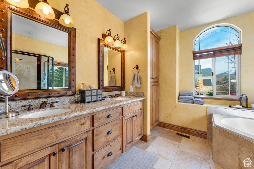 Bathroom featuring tile flooring, double sink, large vanity, and tiled tub