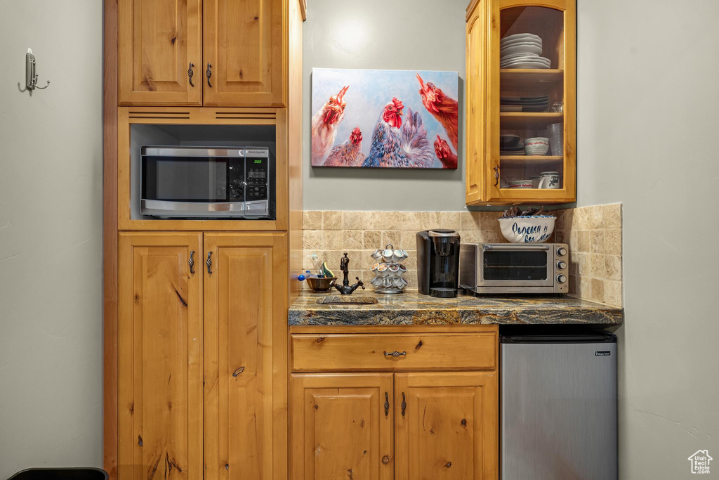 Kitchen featuring dark stone counters, backsplash, and refrigerator