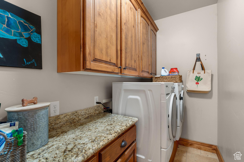 Clothes washing area featuring cabinets, light tile floors, and washer and clothes dryer