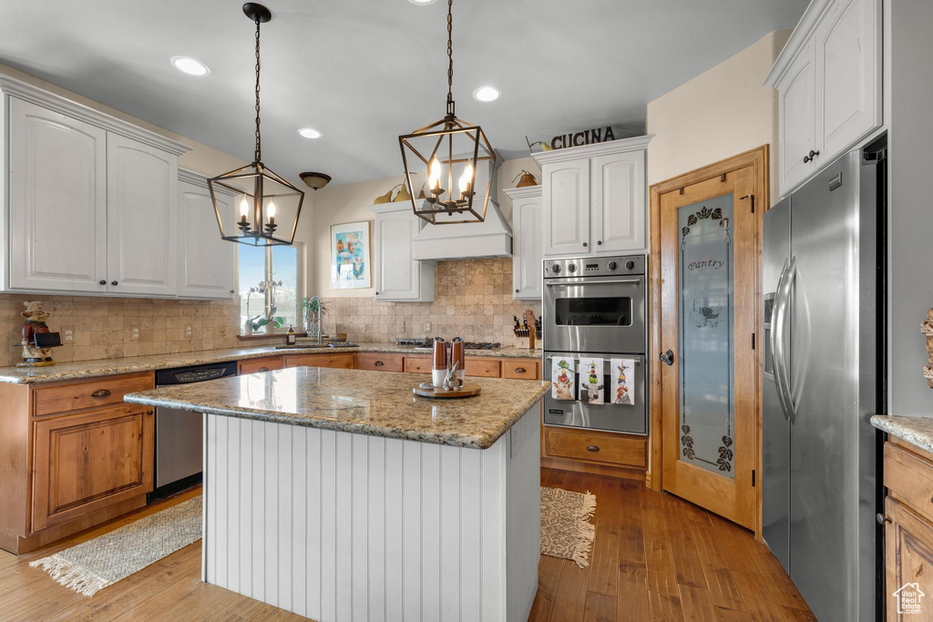Kitchen with light stone counters, white cabinets, stainless steel appliances, light wood-type flooring, and a center island