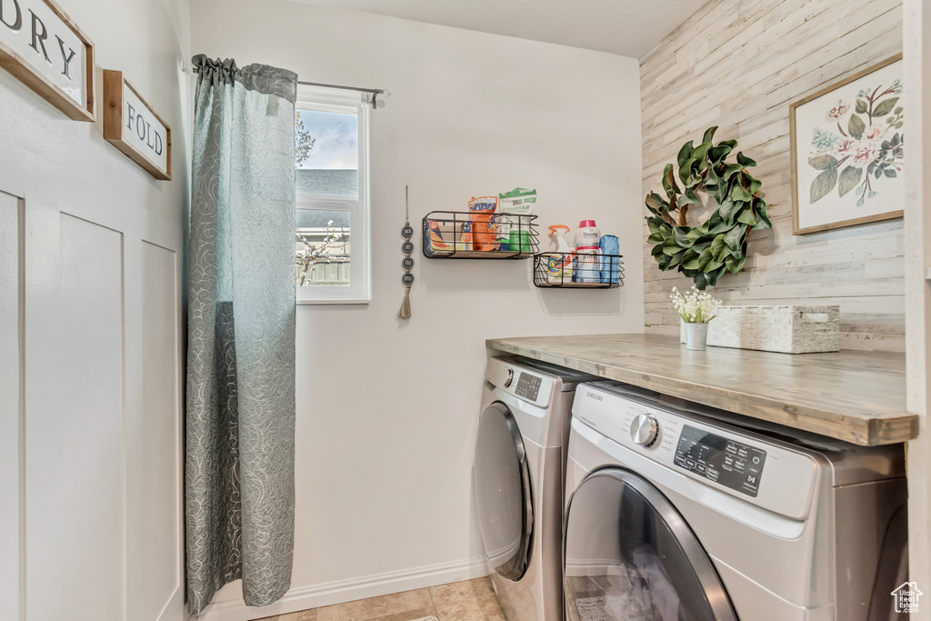 Laundry area featuring light tile floors, wood walls, and washer and dryer