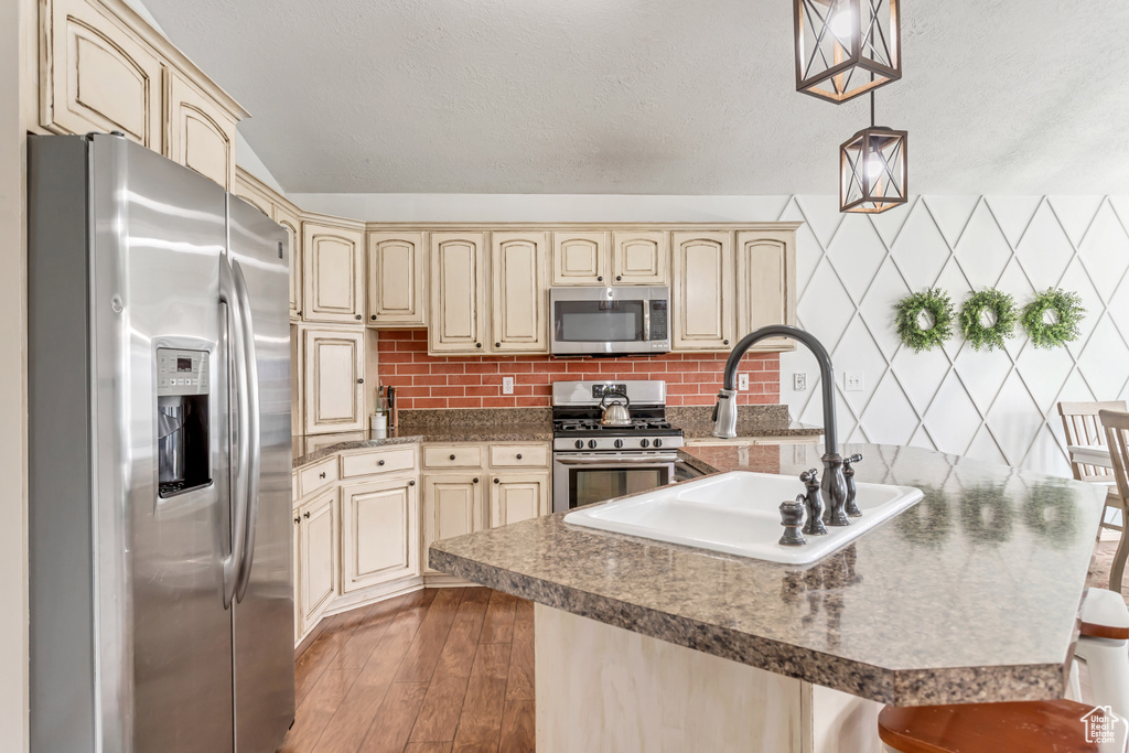 Kitchen featuring decorative light fixtures, a breakfast bar, hardwood / wood-style floors, appliances with stainless steel finishes, and backsplash