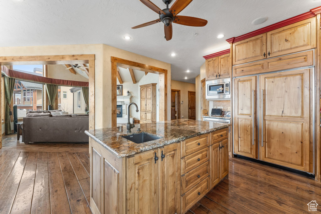 Kitchen featuring dark hardwood / wood-style flooring, ceiling fan, built in appliances, and an island with sink