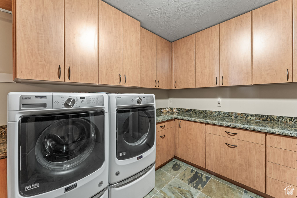 Laundry area featuring washing machine and clothes dryer, cabinets, a textured ceiling, and light tile floors