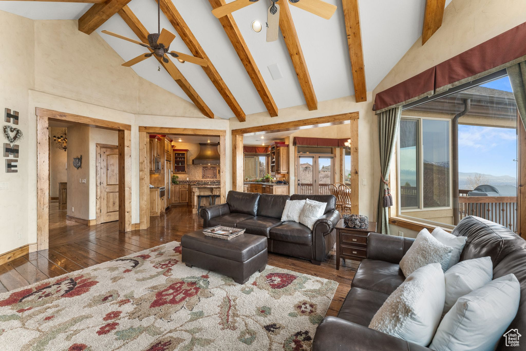 Living room featuring dark wood-type flooring, ceiling fan, high vaulted ceiling, and beam ceiling