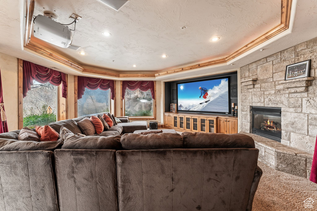 Home theater with a tray ceiling, a stone fireplace, and crown molding