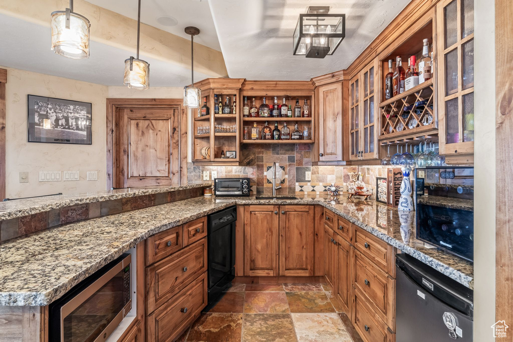 Kitchen featuring light stone counters, hanging light fixtures, stainless steel microwave, dishwasher, and tile floors