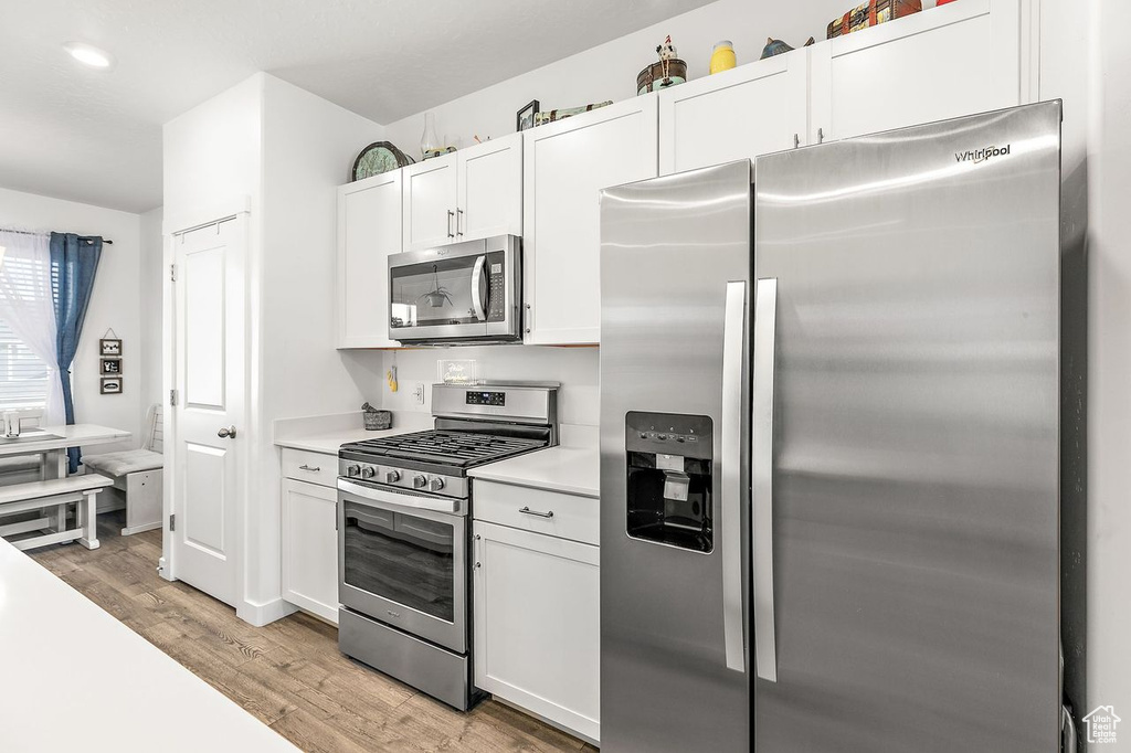 Kitchen with white cabinets, light hardwood / wood-style floors, and stainless steel appliances