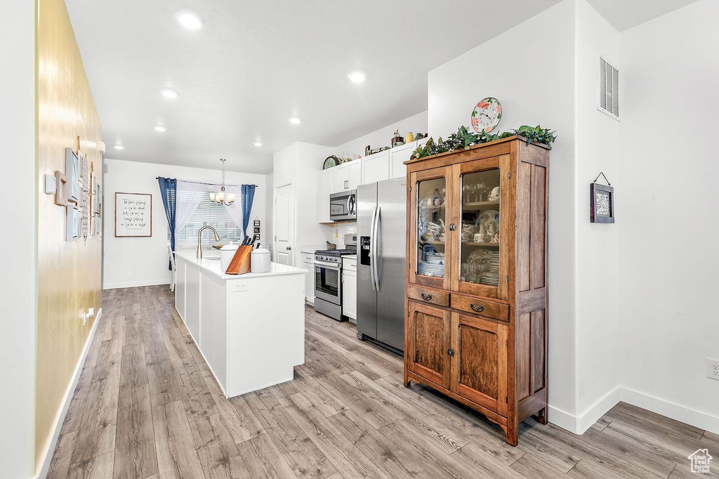 Kitchen with light hardwood / wood-style floors, stainless steel appliances, decorative light fixtures, a kitchen island with sink, and an inviting chandelier