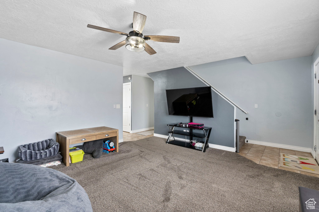 Game room with ceiling fan, dark colored carpet, and a textured ceiling