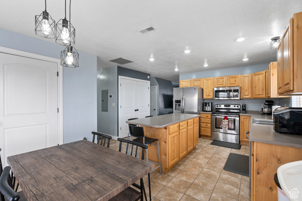 Kitchen with a kitchen island, light tile flooring, stainless steel appliances, and pendant lighting