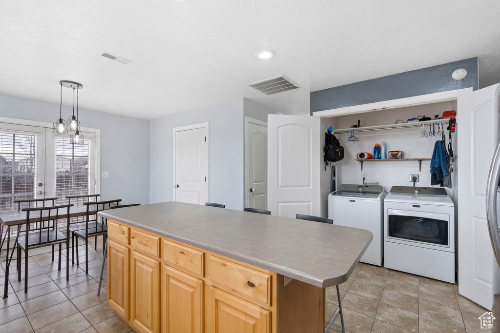 Kitchen featuring washer and clothes dryer, light brown cabinets, light tile flooring, and a center island