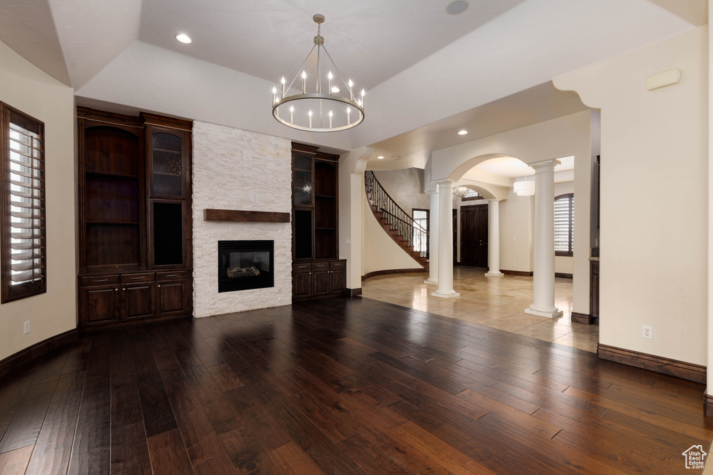 Unfurnished living room featuring tile floors, a fireplace, ornate columns, a notable chandelier, and lofted ceiling