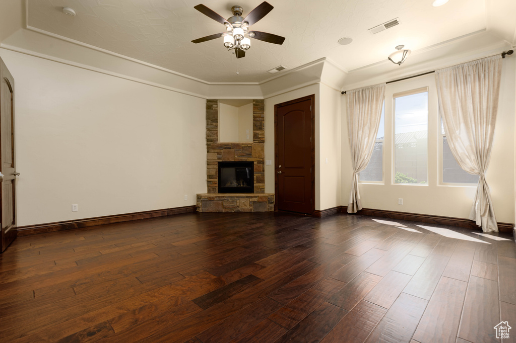 Unfurnished living room featuring ceiling fan, crown molding, a fireplace, a tray ceiling, and dark wood-type flooring