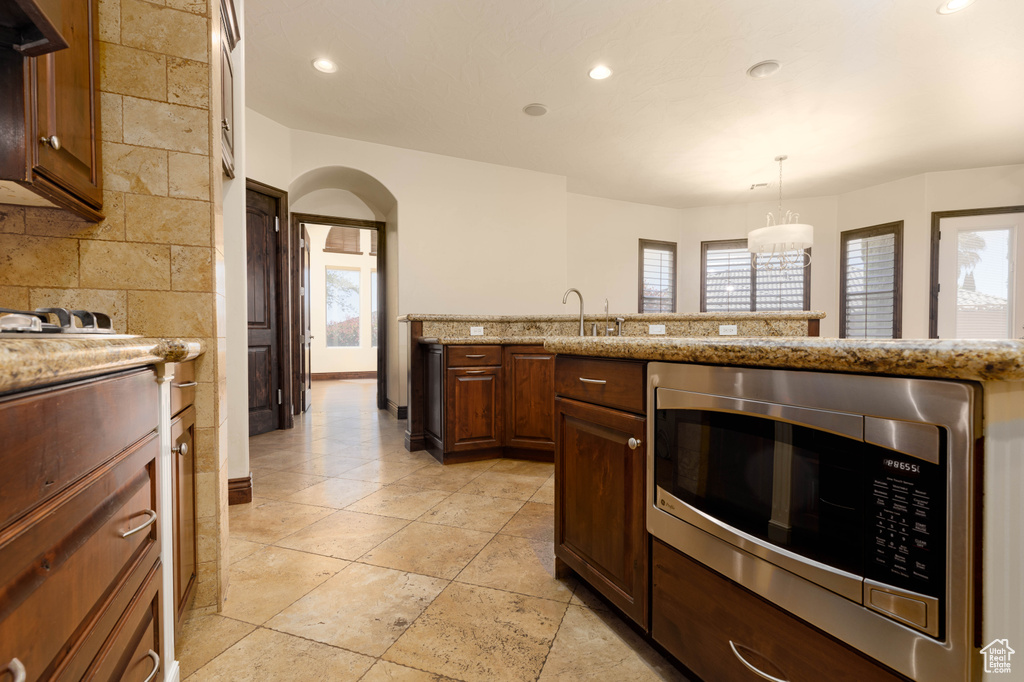 Kitchen with light tile flooring, pendant lighting, stainless steel microwave, light stone counters, and sink