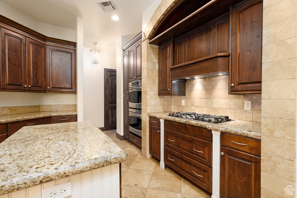 Kitchen featuring gas stovetop, light tile floors, backsplash, custom range hood, and light stone counters