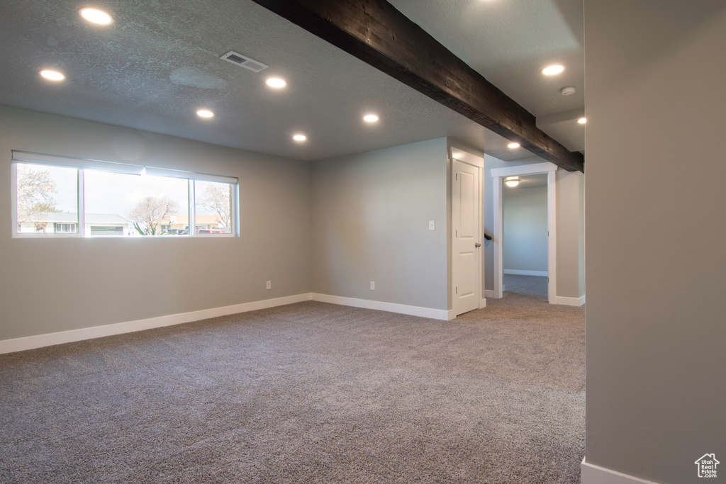 Spare room featuring beam ceiling, light carpet, and a textured ceiling
