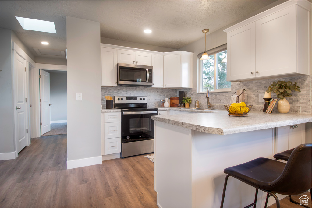 Kitchen with appliances with stainless steel finishes, a skylight, decorative light fixtures, and white cabinetry