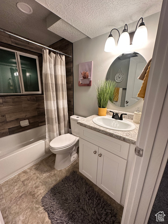 Full bathroom featuring toilet, oversized vanity, shower / bath combo, a textured ceiling, and tile floors
