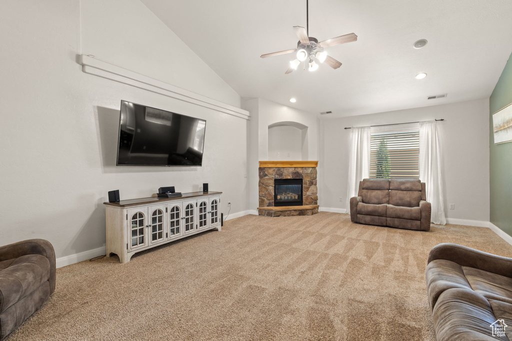 Living room with lofted ceiling, light colored carpet, a stone fireplace, and ceiling fan
