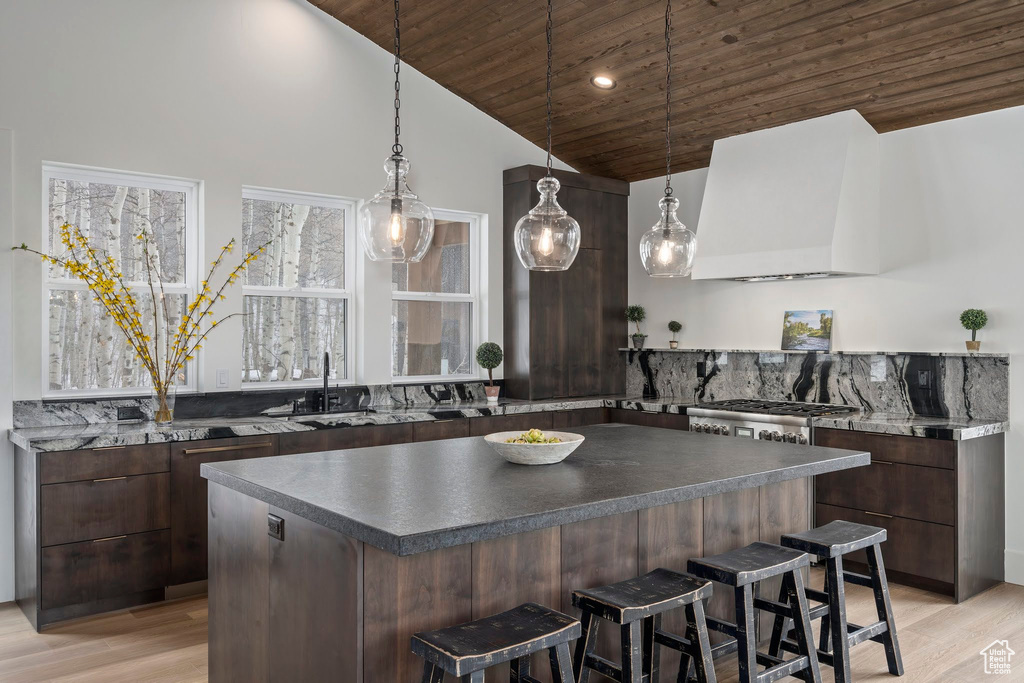 Kitchen featuring dark brown cabinetry, custom exhaust hood, a kitchen island, a breakfast bar, and wood ceiling