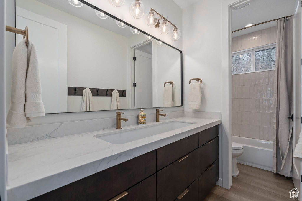 Full bathroom featuring wood-type flooring, vanity, shower / tub combo, and toilet