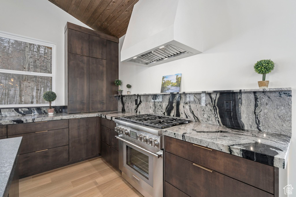 Kitchen featuring tasteful backsplash, vaulted ceiling, light hardwood / wood-style flooring, premium range hood, and stainless steel range