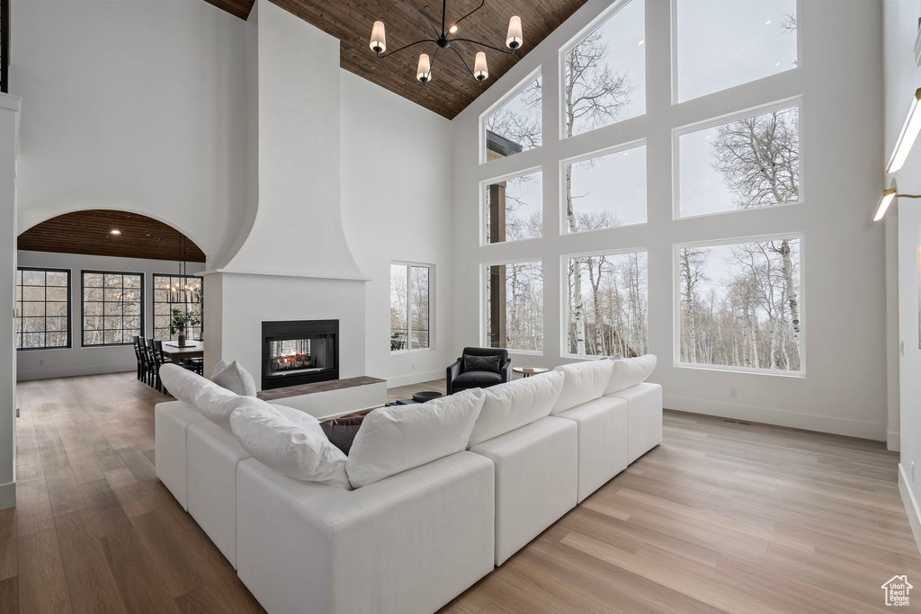 Living room with high vaulted ceiling, wooden ceiling, a fireplace, a notable chandelier, and light wood-type flooring