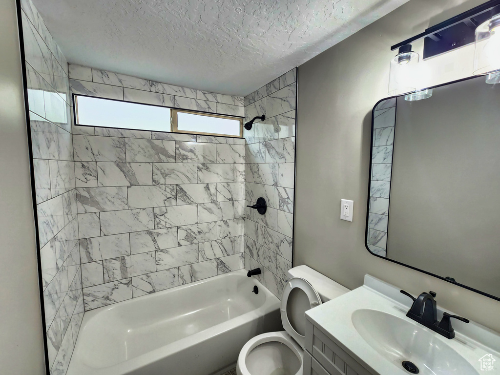 Full bathroom featuring tiled shower / bath, toilet, vanity, and a textured ceiling