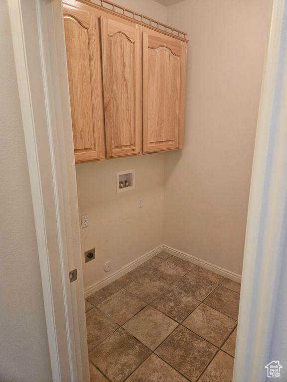 Clothes washing area with hookup for a washing machine, cabinets, light tile flooring, and electric dryer hookup