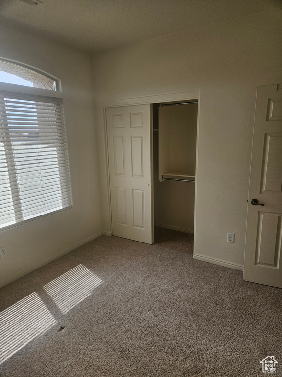 Unfurnished bedroom with a closet, dark colored carpet, and multiple windows