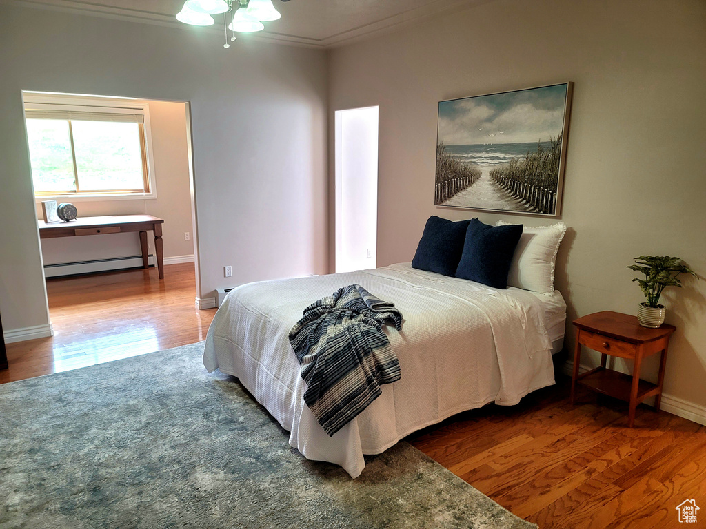 Bedroom with ceiling fan, ornamental molding, hardwood / wood-style flooring, and a baseboard heating unit