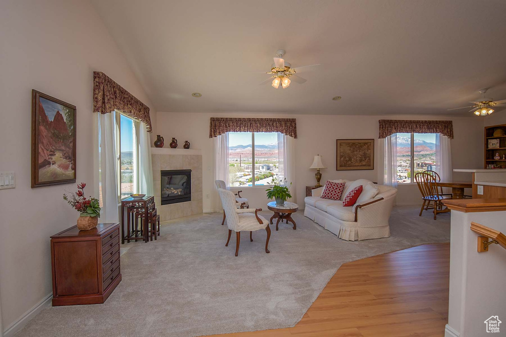 Carpeted living room featuring vaulted ceiling, ceiling fan, a tile fireplace, and a wealth of natural light