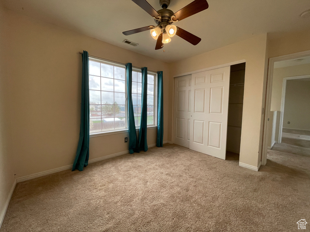 Unfurnished bedroom featuring ceiling fan, a closet, and light colored carpet