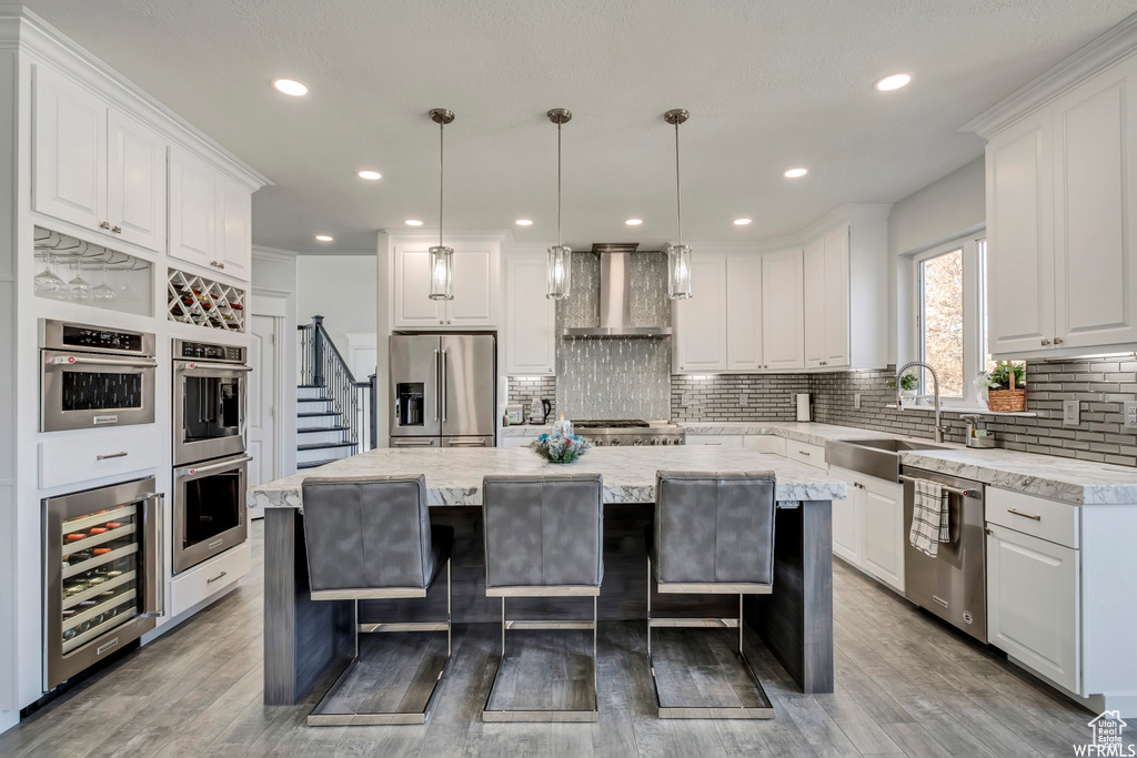 Kitchen featuring appliances with stainless steel finishes, beverage cooler, a center island, wall chimney exhaust hood, and a kitchen breakfast bar