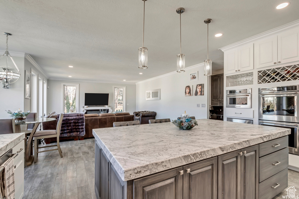 Kitchen with white cabinets, decorative light fixtures, stainless steel double oven, and a kitchen island