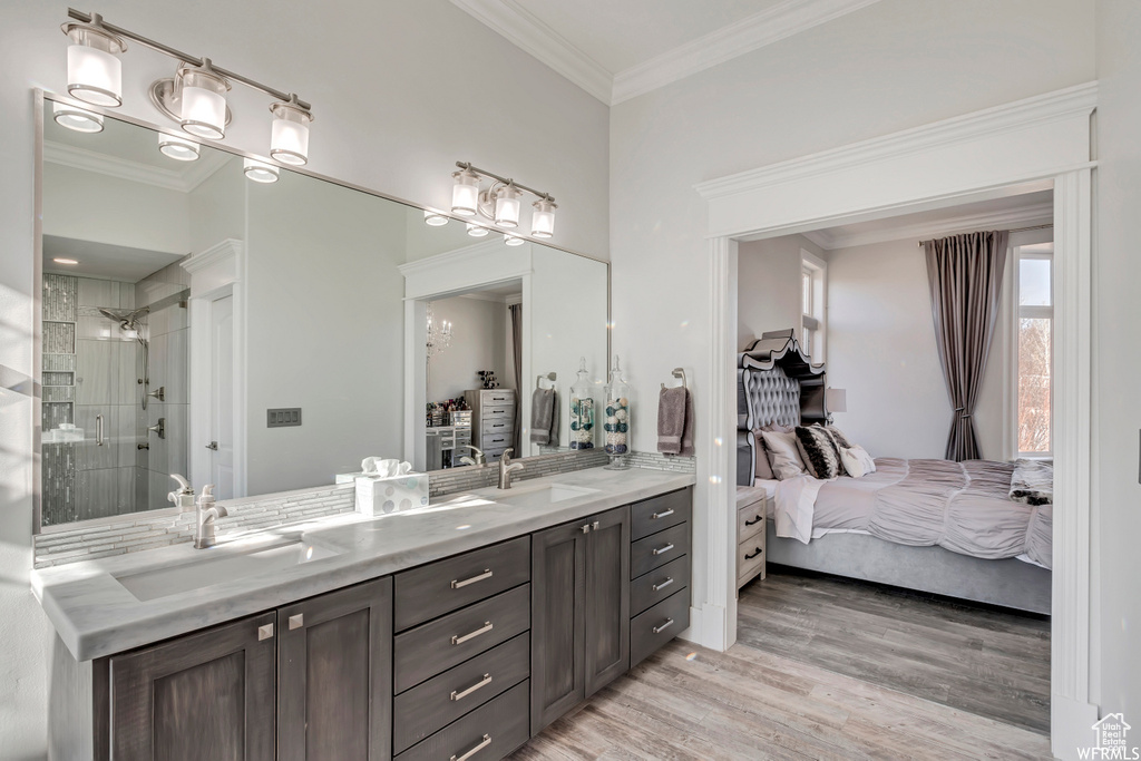Bathroom featuring dual sinks, hardwood / wood-style flooring, crown molding, a tile shower, and vanity with extensive cabinet space