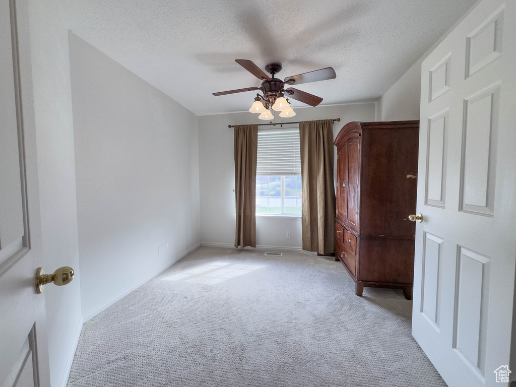 Unfurnished room featuring ceiling fan, a textured ceiling, and light carpet