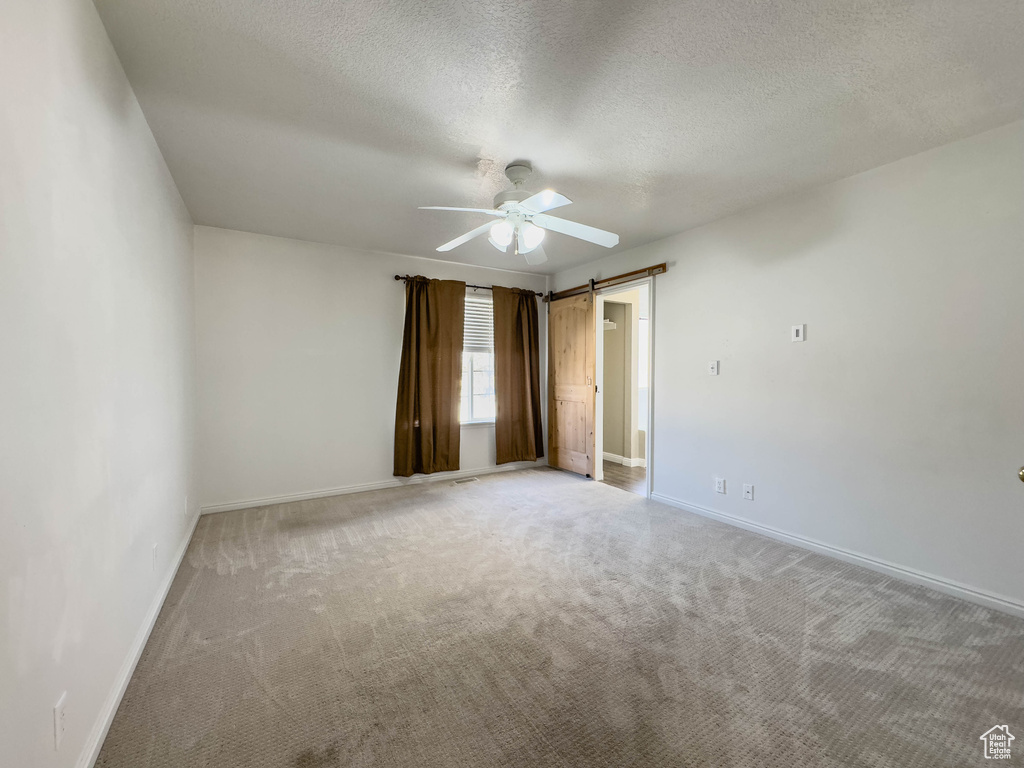 Empty room with a barn door, light carpet, ceiling fan, and a textured ceiling