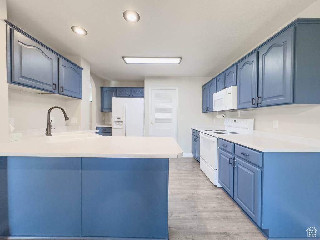 Kitchen with kitchen peninsula, blue cabinets, light hardwood / wood-style flooring, white appliances, and sink