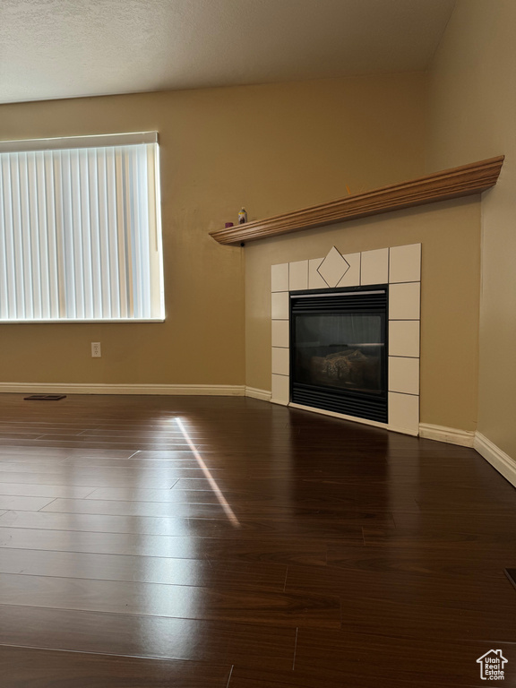 Unfurnished living room with dark wood-type flooring, a textured ceiling, and a tiled fireplace