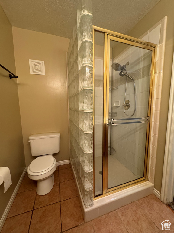 Bathroom with toilet, tile flooring, a shower with shower door, and a textured ceiling
