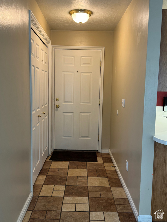 Doorway with dark tile flooring and a textured ceiling