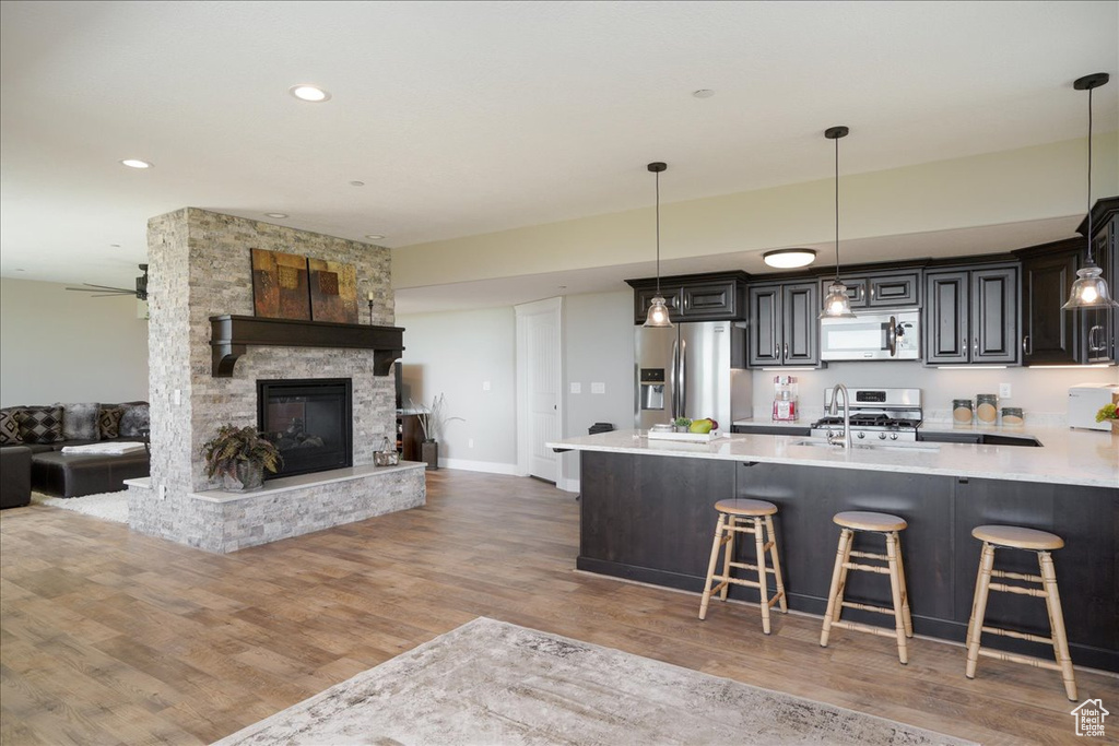 Kitchen featuring a fireplace, a breakfast bar, appliances with stainless steel finishes, hanging light fixtures, and light wood-type flooring