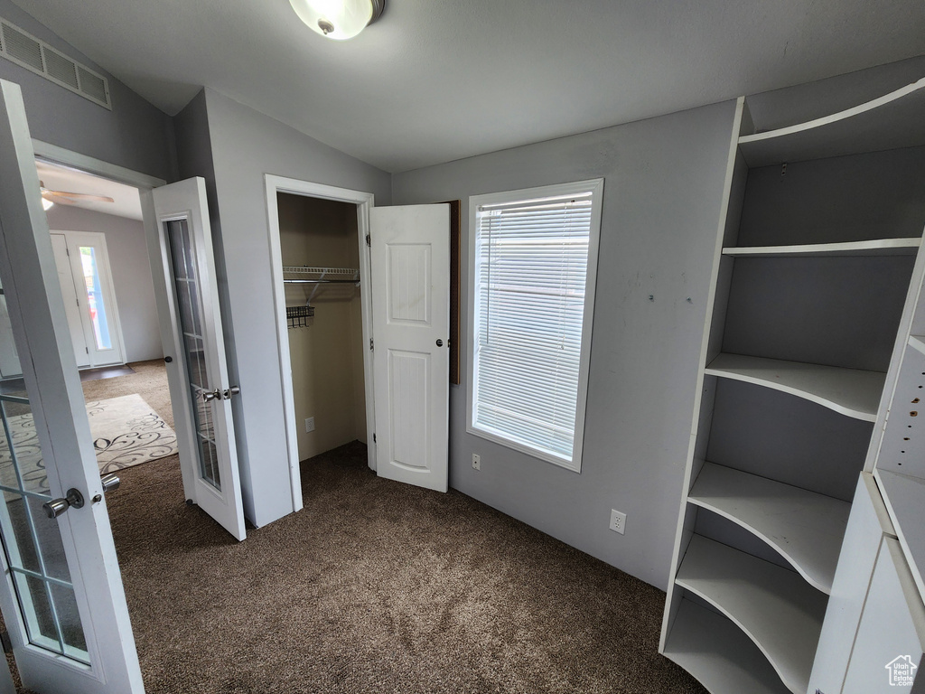Unfurnished bedroom featuring dark carpet, a closet, multiple windows, and french doors