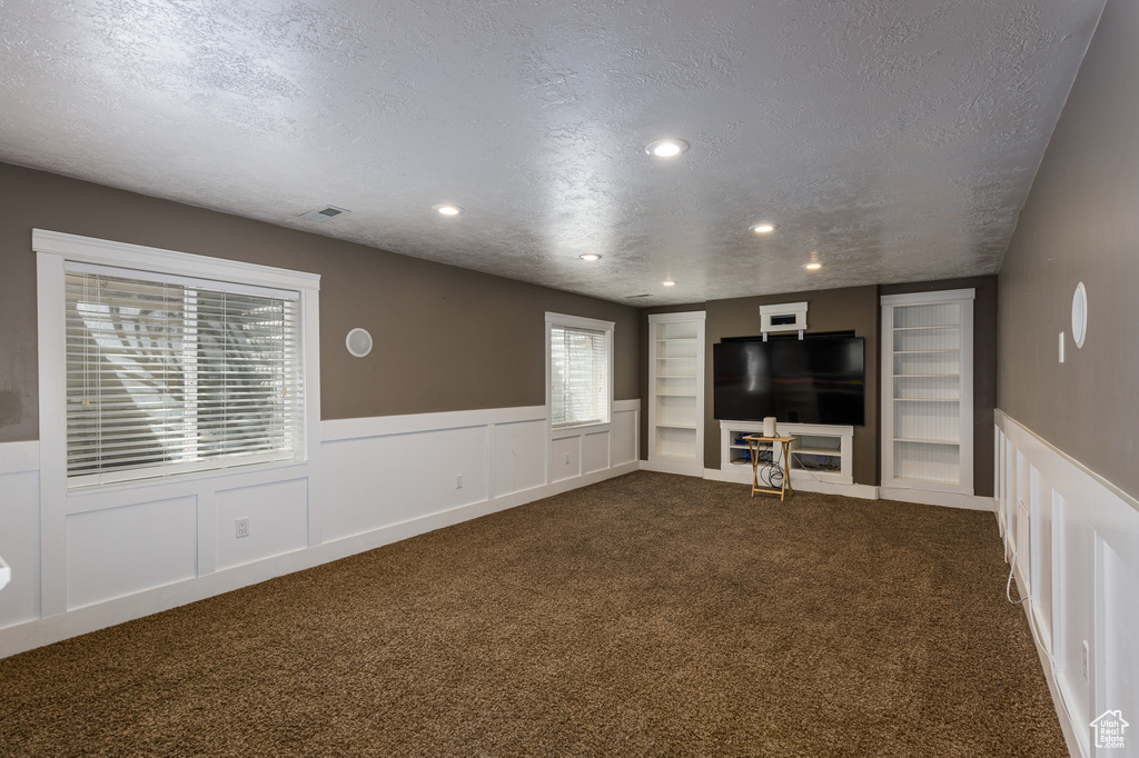 Unfurnished living room featuring built in features, a textured ceiling, and dark carpet