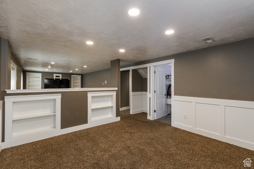 Basement featuring refrigerator, a textured ceiling, and dark carpet